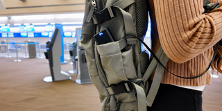 Traveler with portable power bank charging phone from backpack.