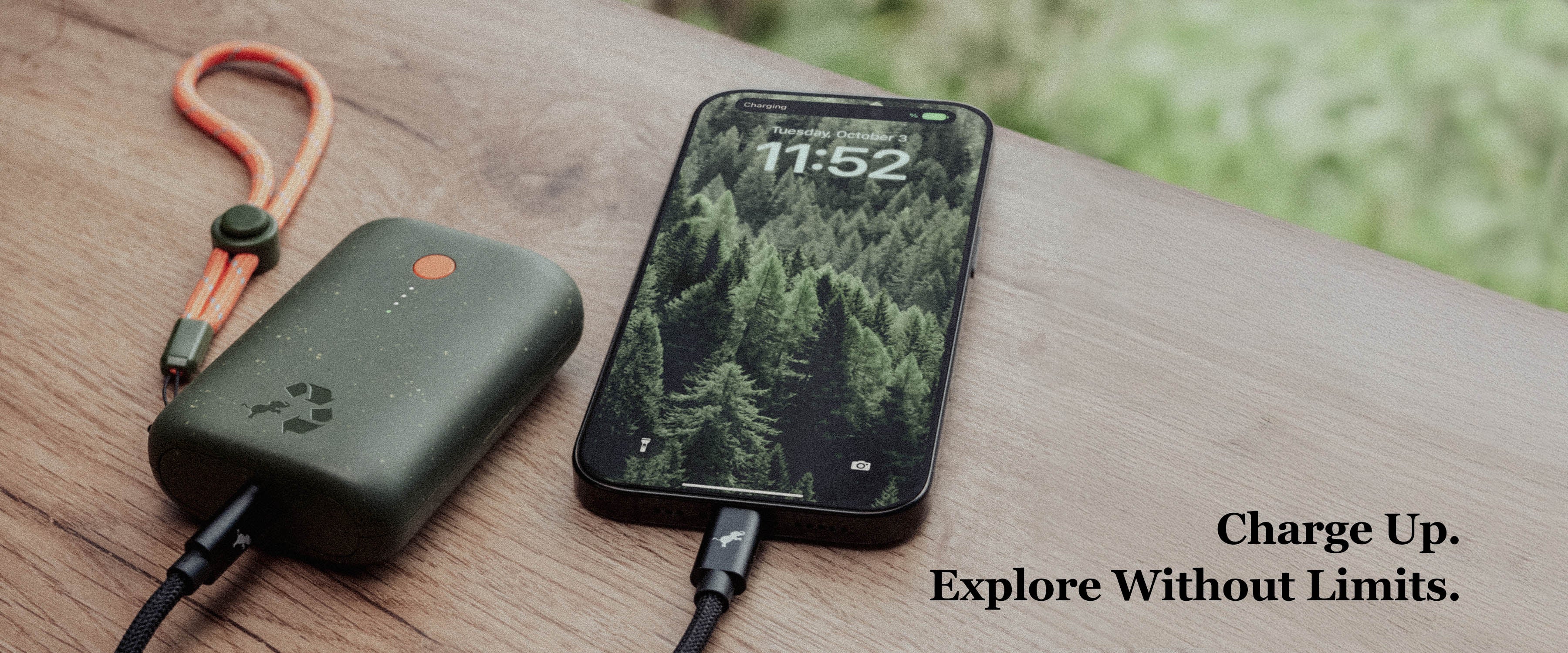 Banner with Green Champ Battery charging an iPhone on wood with greenery in background. Text overlay Charge Up. Explore Without Limits.