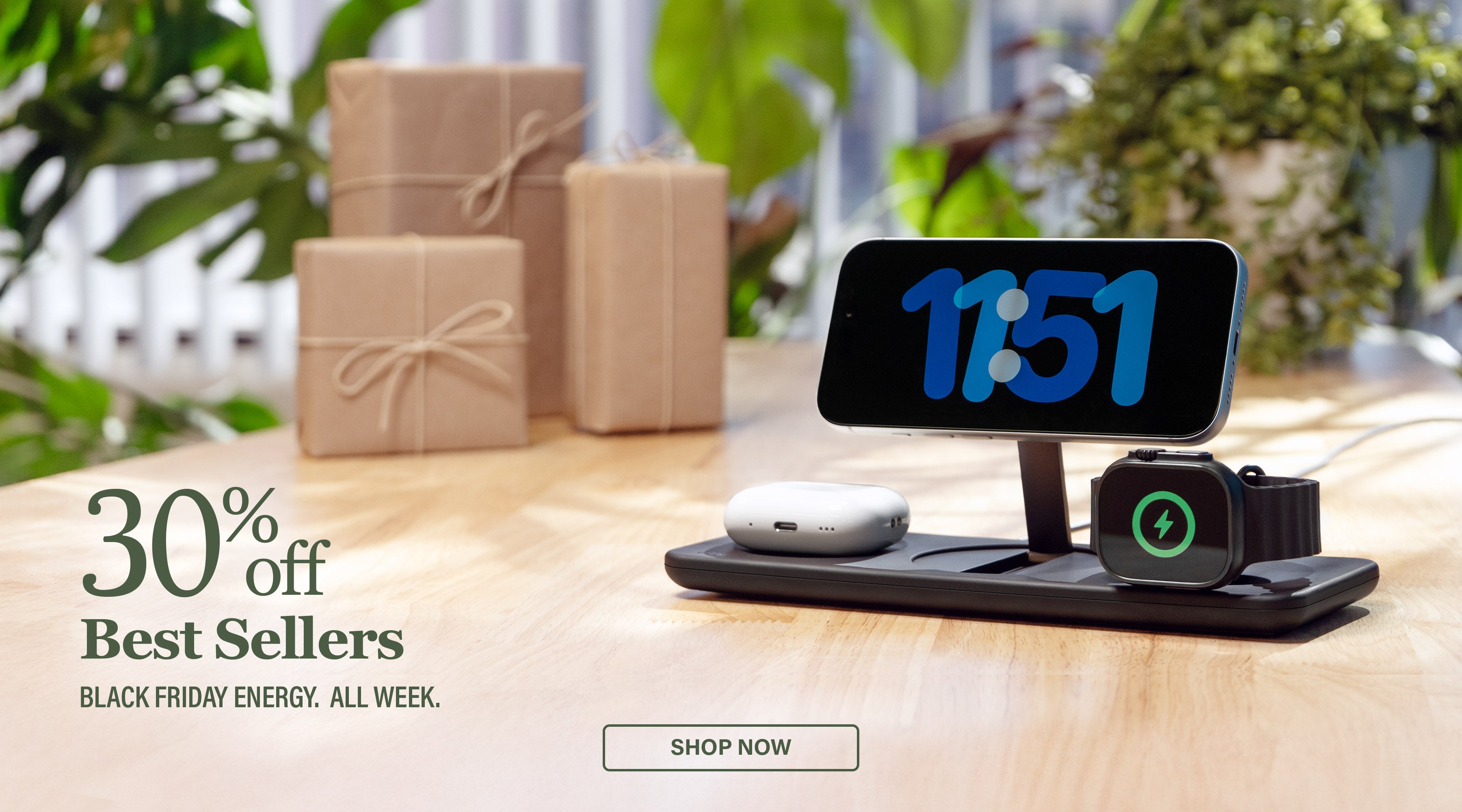 Podium 3-in-1 Wireless charger with clock on screen and Apple Watch and AirPods on a wooden surface with gift boxes and plants in the background. Text reads 30% off Best Sellers Black Friday Energy. All Week.