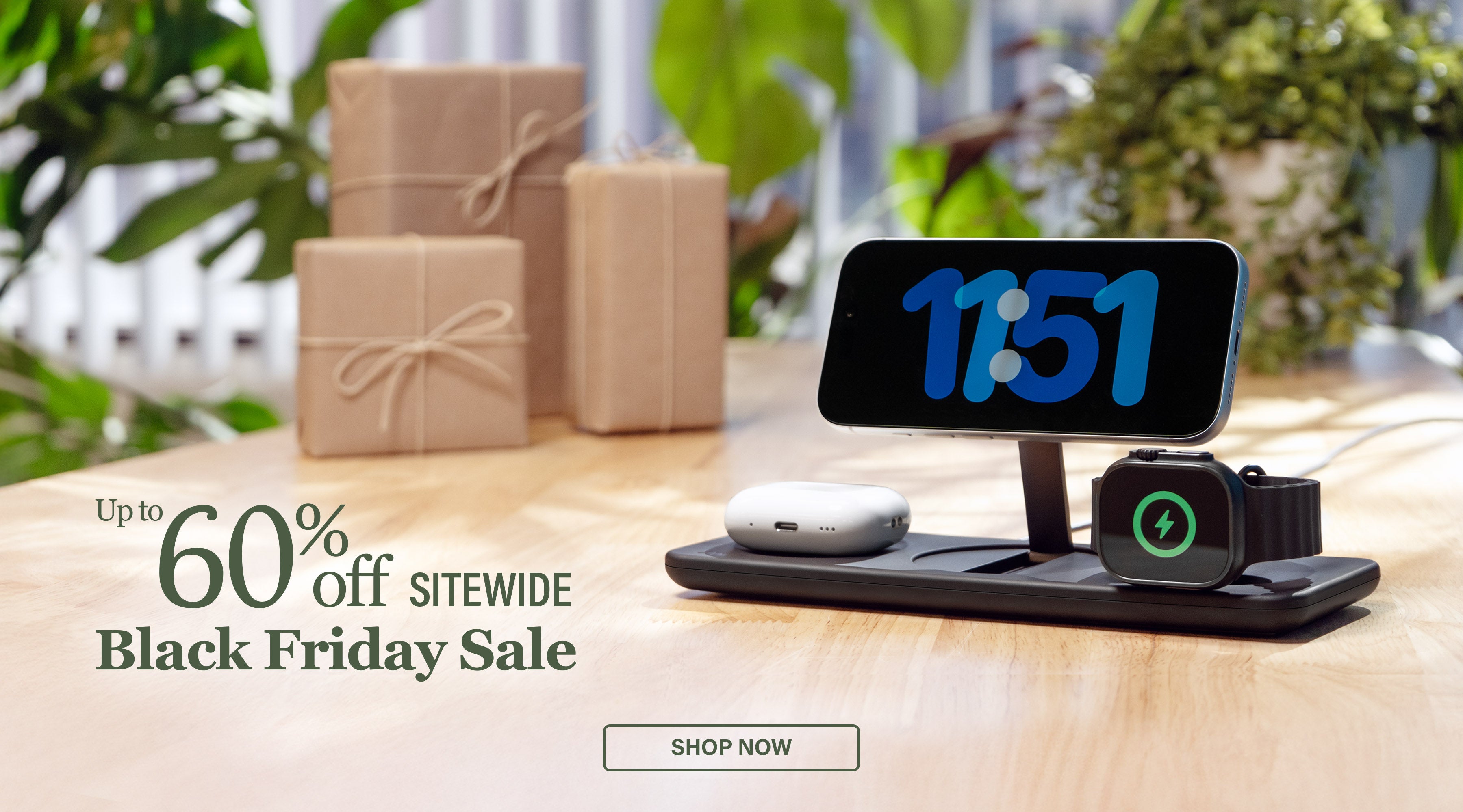 Podium 3-in-1 Wireless charger with clock on screen and Apple Watch and AirPods on a wooden surface with gift boxes and plants in the background. Text reads Up to 60% off Sitewide Black Friday Sale.