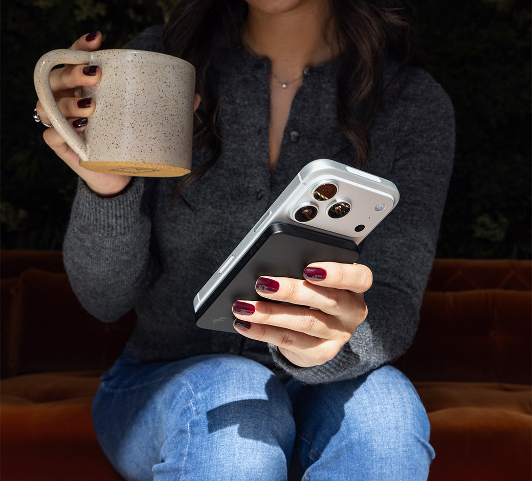 Person holding an iPhone 17 Pro with Champ Wireless magnetically attached and a mug on a dark background.
