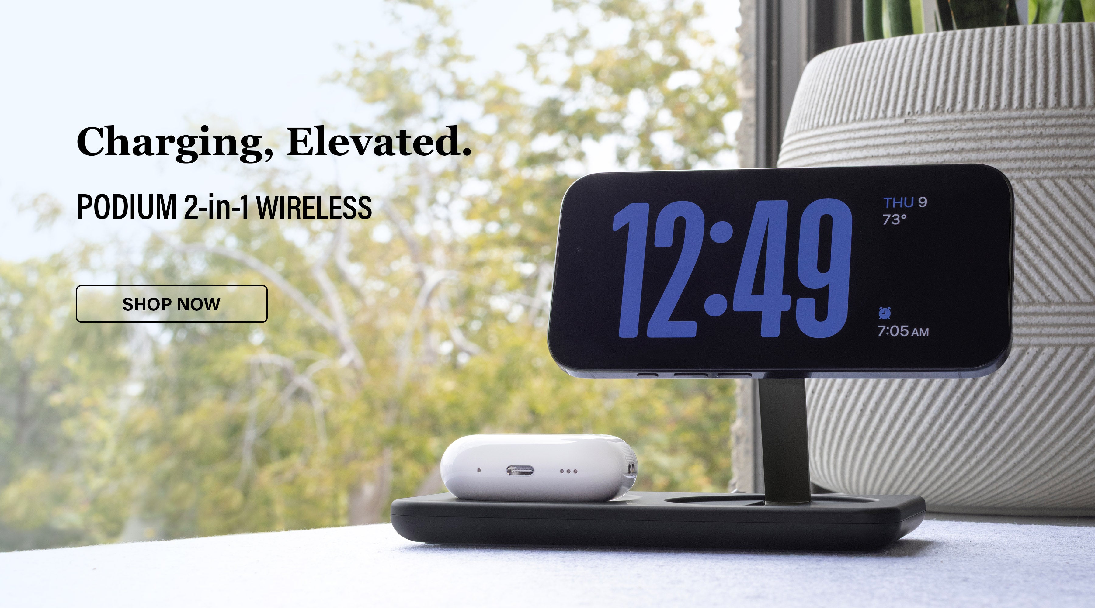 iPhone and AirPods charging on Podium 2-in-1 wireless charger next to window on desk. Text overlay 