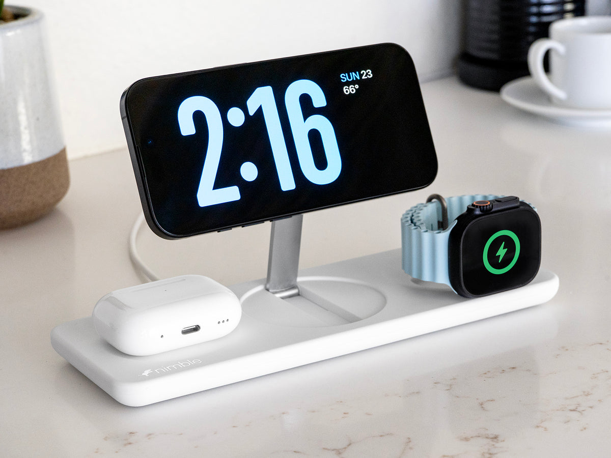 Podium 3-in-1 25W Wireless charging stand with iPhone, AirPods and Apple Watch devices charging upright on a marble surface.