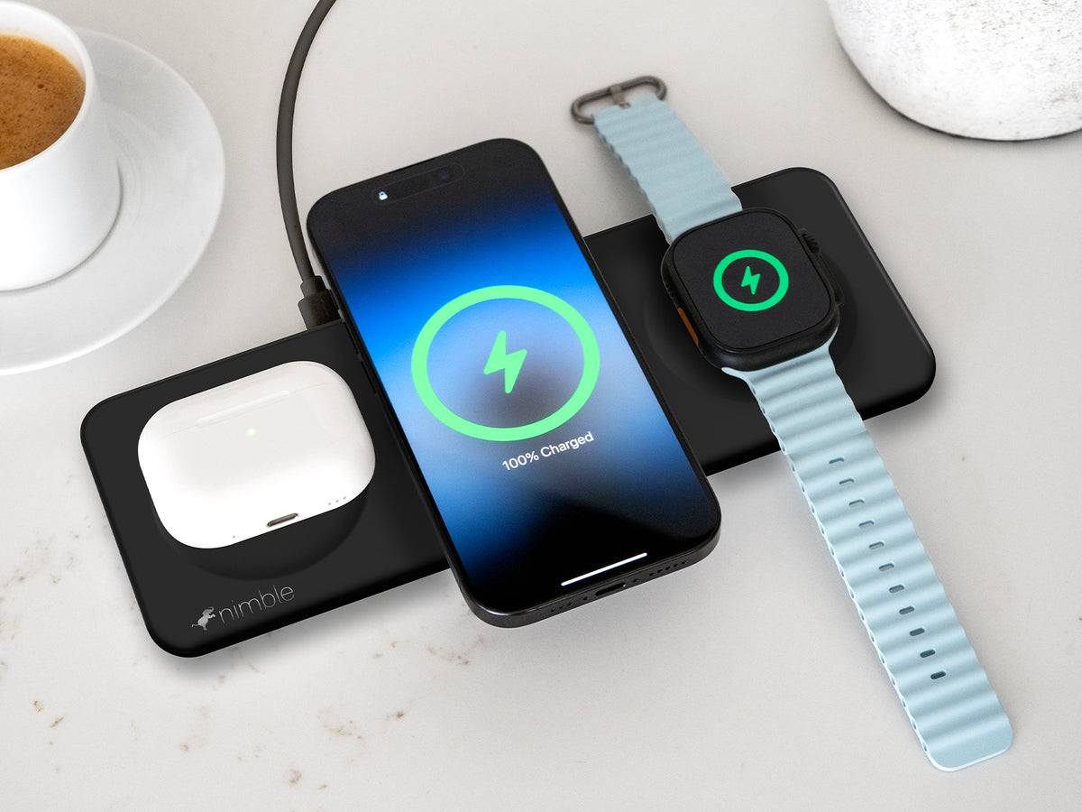 Podium 3-in-1 25W Wireless charging stand with iPhone, AirPods and Apple Watch devices charging on a light surface with a cup of coffee.