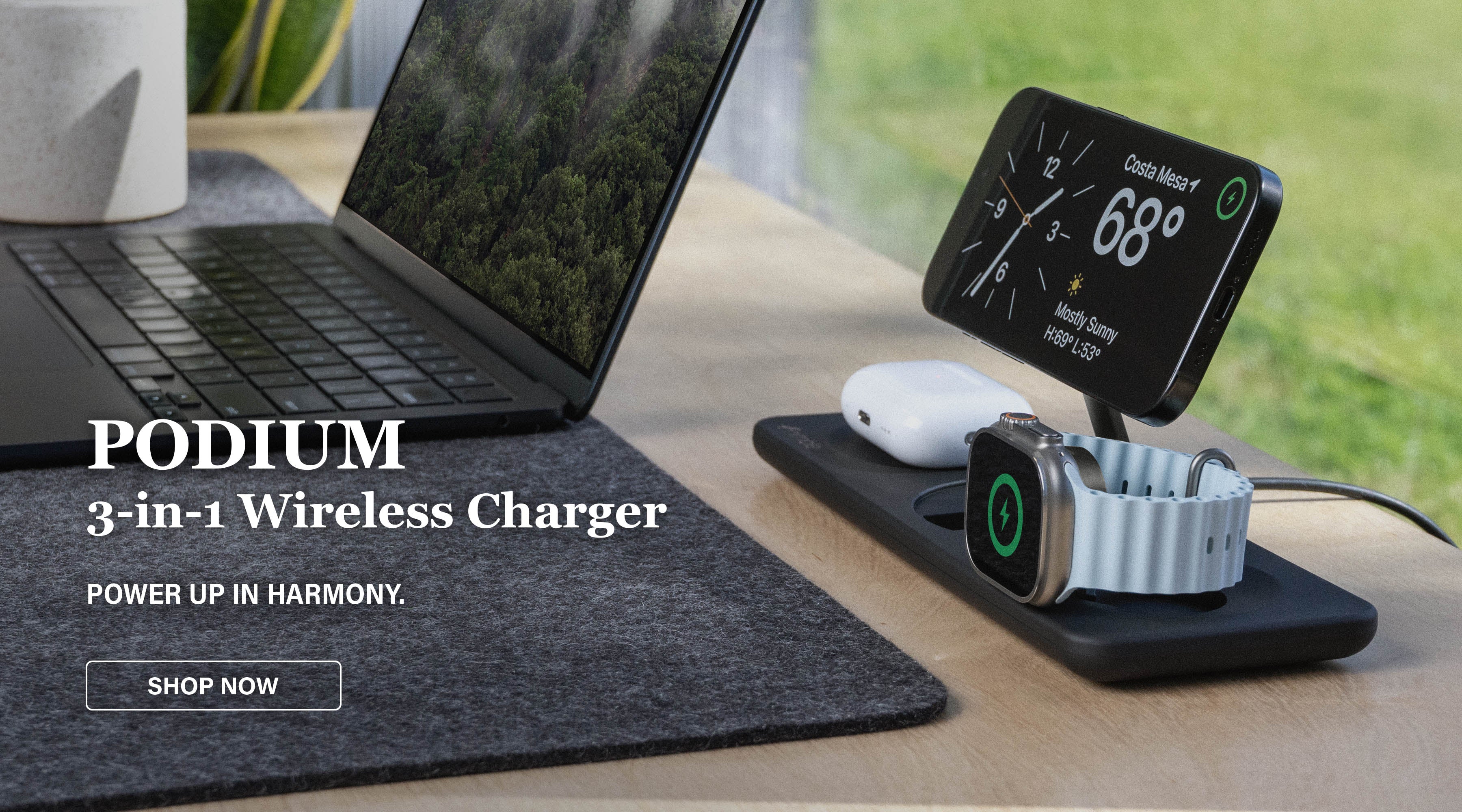 iPhone, Apple Watch, and AirPods charging on Black Podium 3-in-1 Wireless Charger near window on desk with Macbook. Text overlay “PODIUM 3-in-1 Wireless Charger POWER UP IN HARMONY. SHOP NOW.