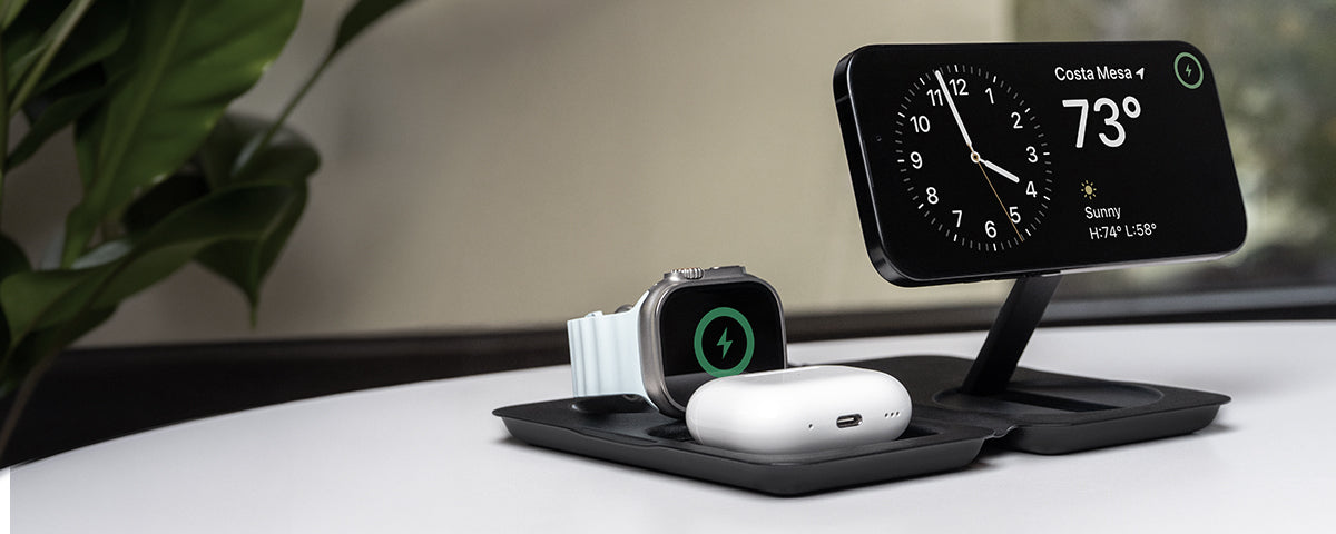 iPhone with a clock app displaying temperature, Apple Watch, and AirPods on Fold 3-in-1 wireless charger on a desk.