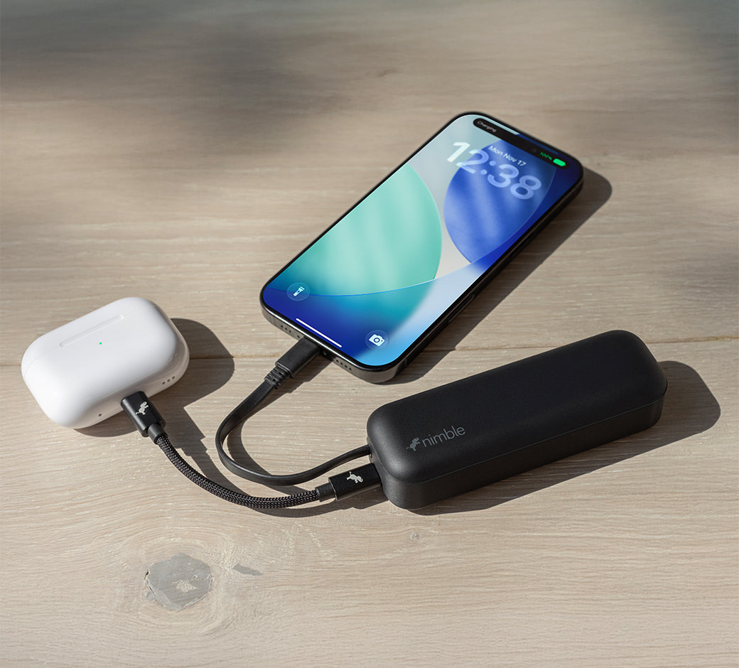 Smartphone and AirPods connected to a black Wally Pro 20 wall charger with built-in battery on a wooden surface.