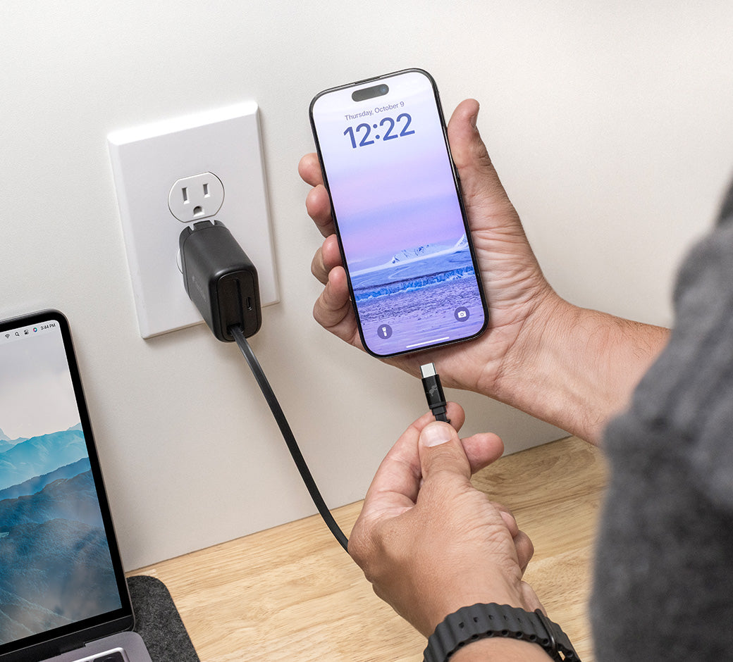Person plugging an iPhone into the Wally Stretch retractable cable, with a laptop on a desk in the background.